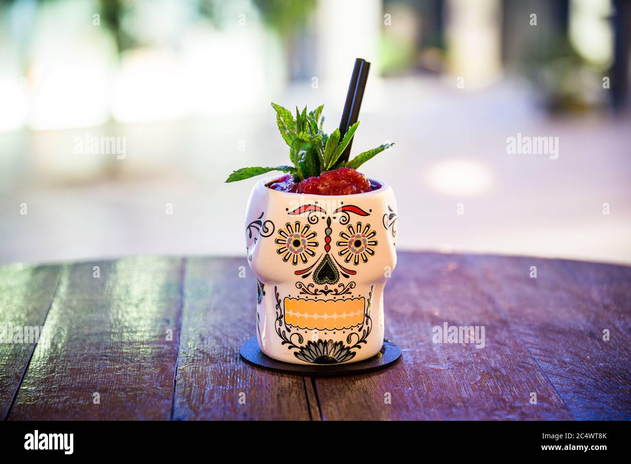 Sie können ein weißes Cocktailglas mit einem Gesicht sehen, das darauf aufgedruckt ist das Glas befindet sich auf einem Holztisch und der Hintergrund des Bildes ist nicht fokussiert Stockfoto