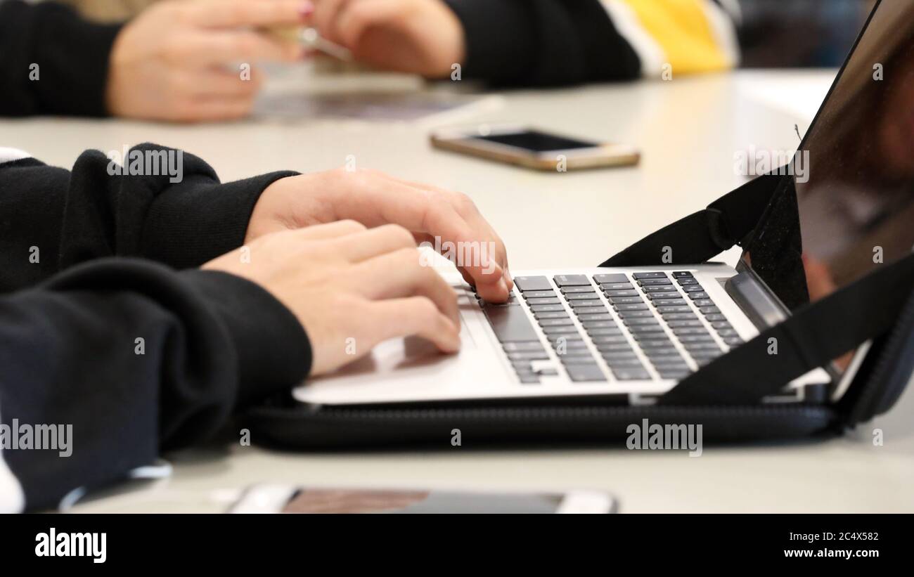 Der moderne Lernende. Ein Schüler in einem High School Klassenzimmer Umgebung tippen auf einem Computer oder Laptop-Tastatur mit Telefonen in der Nähe. Stockfoto