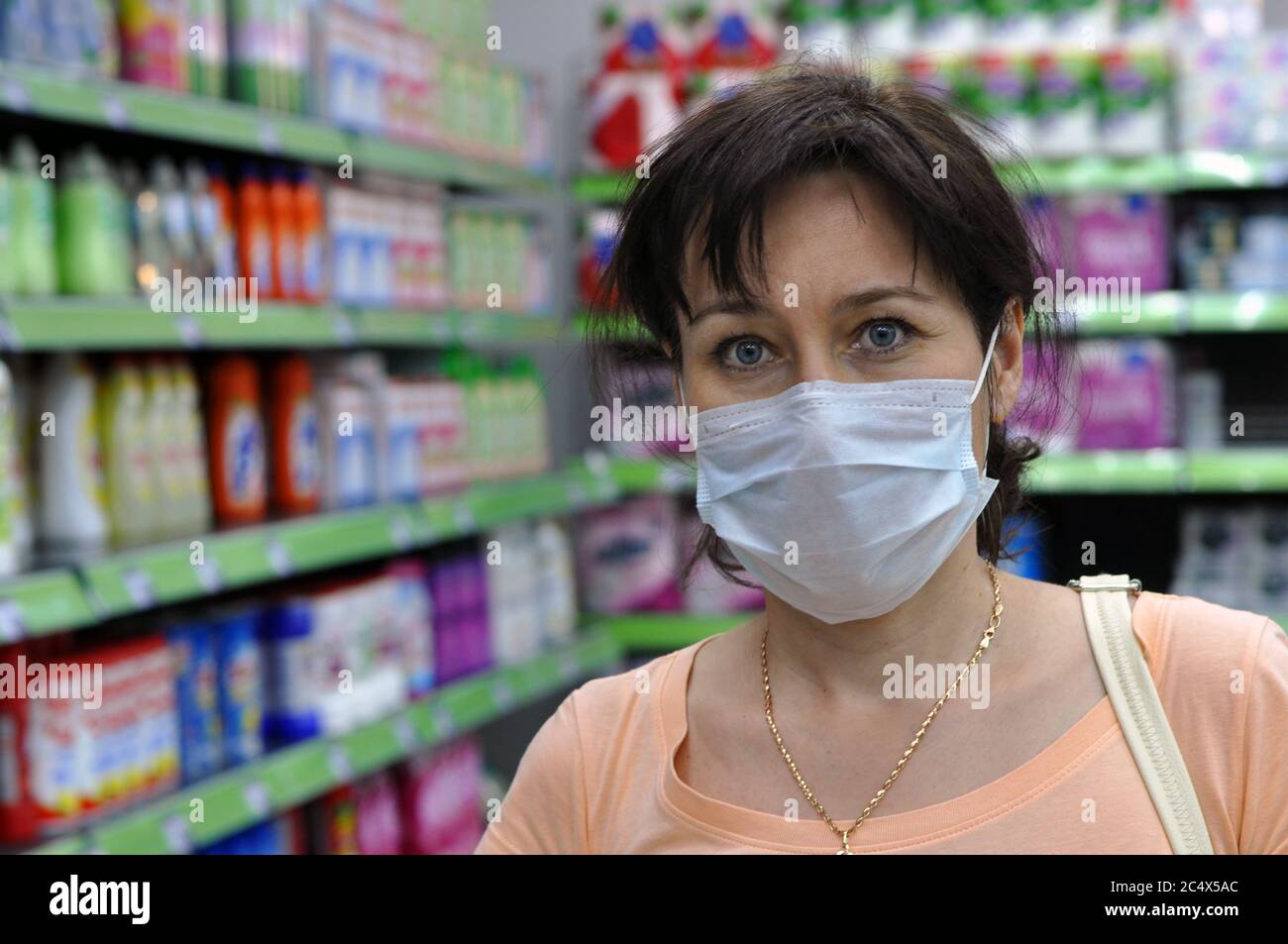 Junge Frau mit einer medizinischen Maske in einem Supermarkt und Blick auf die Kamera. Das Konzept des Schutzes gegen Coronavirus und andere respiratorische Stockfoto