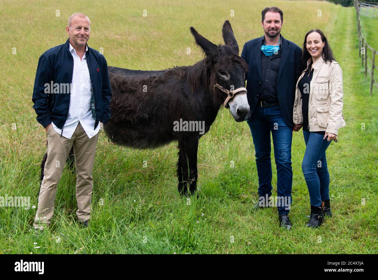 29. Juni 2020, Bayern, Weßling: Heino Ferch (l-r), Schauspieler, Tamer Martin Lacey und Jana Mandana Lacey-Krone nehmen an einer Pressetour auf dem Bauernhof Circus Krone Teil und stehen neben einem Esel. Der Hof beherbergt in der Regel alte Zirkustiere. Aufgrund der aktuellen Situation verbringen einige aktive Tiere in diesem Jahr auch den Sommer auf dem Bauernhof. Foto: Sven Hoppe/dpa Stockfoto