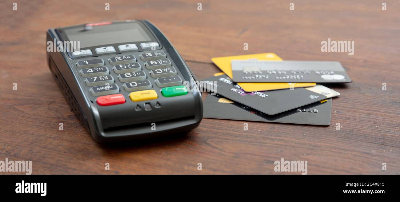 POS-Terminal und Kreditkarten auf Holzhintergrund, Banner. Terminal Kassenautomat für kontaktloses Bezahlen. Bankausstattung, Konsumdenken, sh Stockfoto