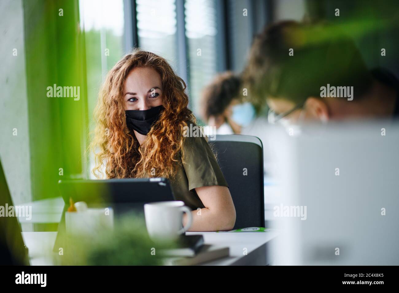 Junge Frau mit Gesichtsmaske wieder bei der Arbeit im Büro nach Lockdown. Stockfoto