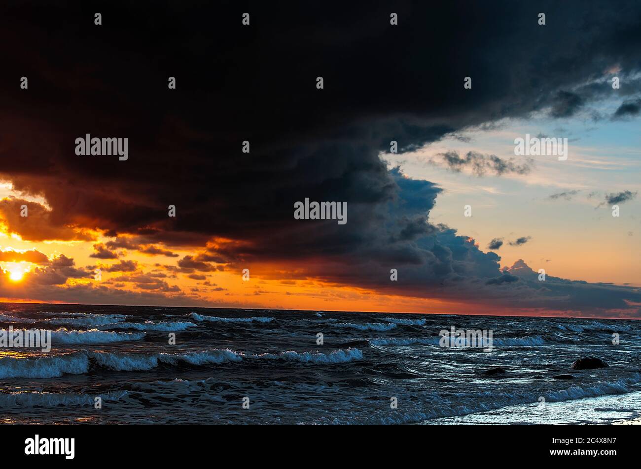Das stürmische Meer, die dunkle bogenförmige Wolke über den meisten Himmel, die Sonne bei Sonnenuntergang färbt den Himmel mit einem dramatisch leuchtend gelb-roten Licht Stockfoto
