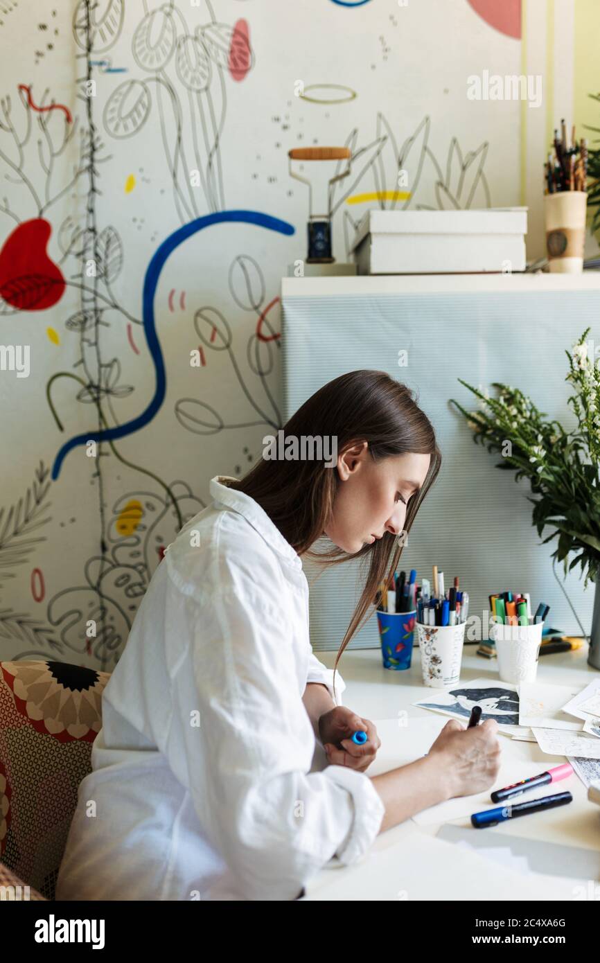 Junger Maler im Hemd am Schreibtisch verträumt Zeichnung mit großen Mustern Leinwand auf Hintergrund zu Hause Stockfoto