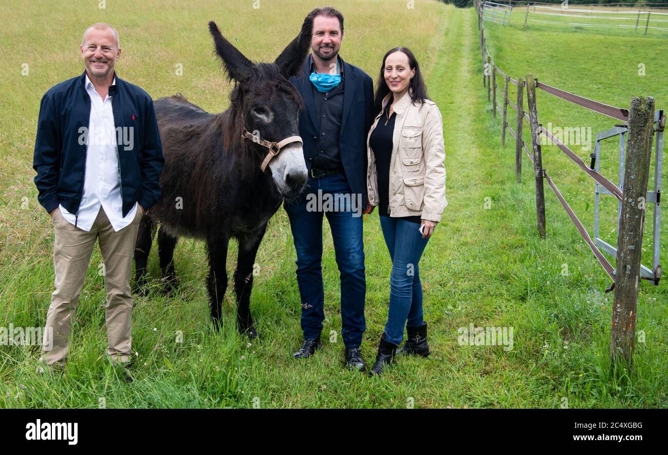 29. Juni 2020, Bayern, Weßling: Heino Ferch (l-r), Schauspieler, Tamer Martin Lacey und Jana Mandana Lacey-Krone nehmen an einer Pressetour auf dem Bauernhof Circus Krone Teil und stehen neben einem Esel. Der Hof beherbergt in der Regel alte Zirkustiere. Aufgrund der aktuellen Situation verbringen einige aktive Tiere in diesem Jahr auch den Sommer auf dem Bauernhof. Foto: Sven Hoppe/dpa Stockfoto