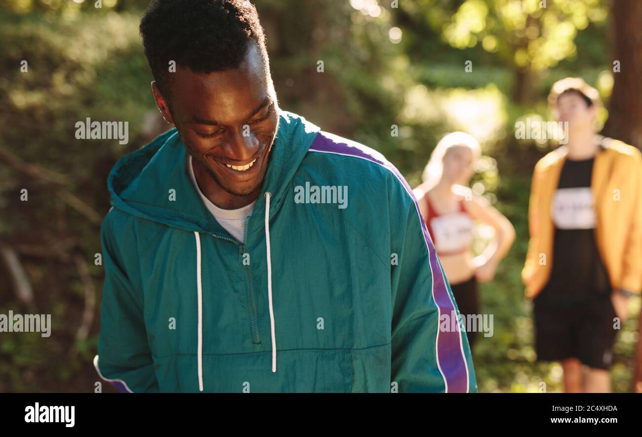 Afrikanischer Sportler, der auf dem Bergweg steht und mit Menschen im Hintergrund lächelt. Stockfoto