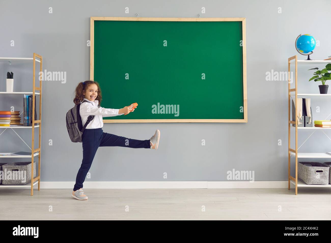 Zurück zur Schule. Lustige Schülerin mit einem Buch ist zu Fuß auf dem Hintergrund der Schule Tafel. Stockfoto