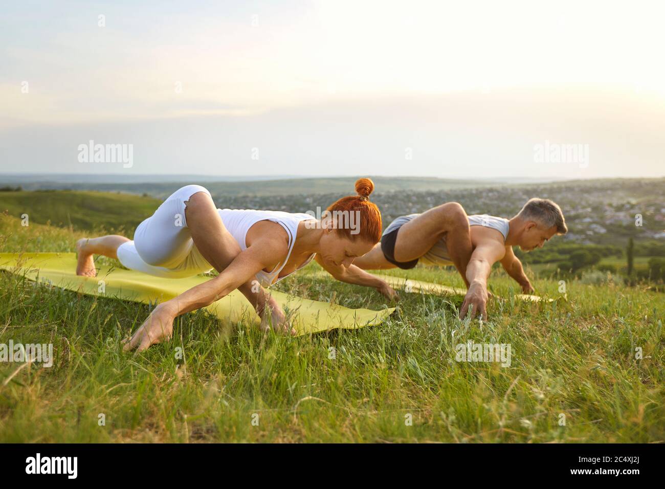 Junges Paar, das gemeinsam Yoga in den Bergen macht. Starker Mann und Frau, die in der Natur die Ausfallsstellung des Läufers ausführen Stockfoto