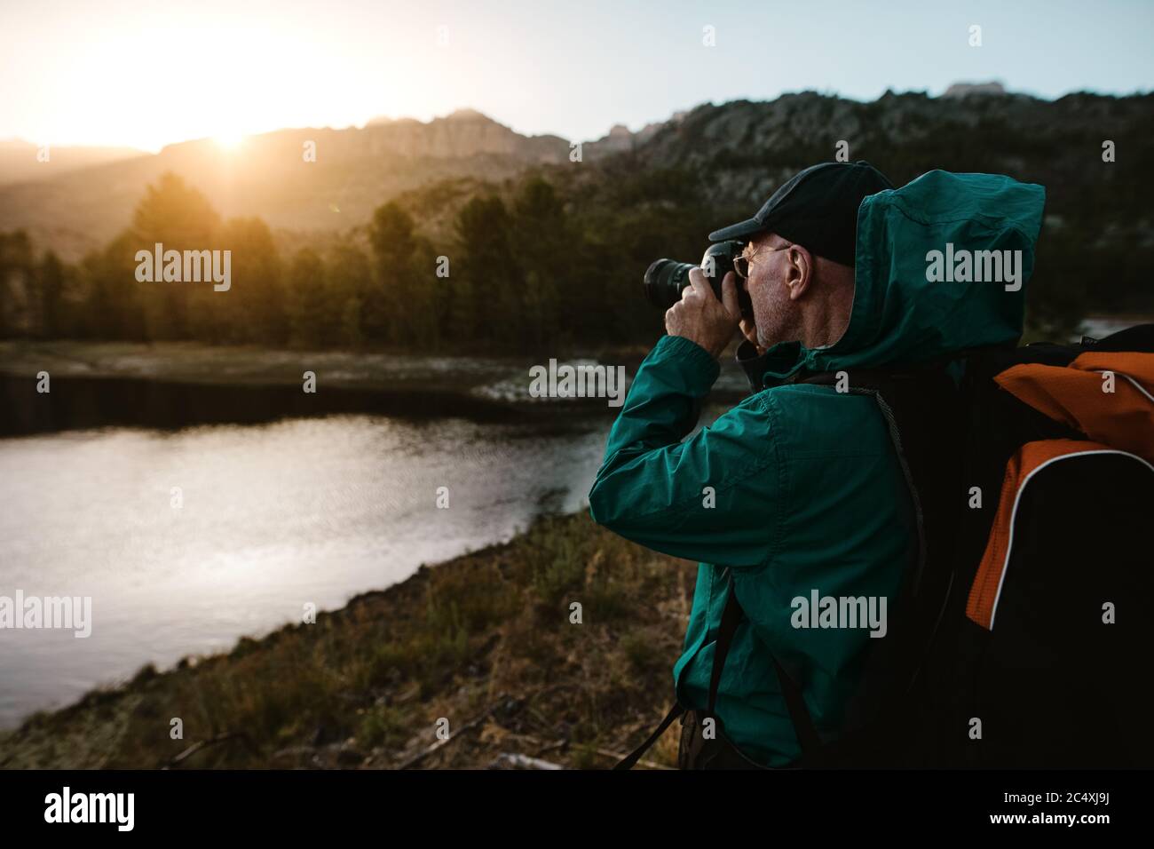 Alter Mann auf Wanderurlaub fotografieren schöne Aussicht mit einer Digitalkamera. Älterer Mann am Fluss im Wald stehen und Fotos machen. Stockfoto