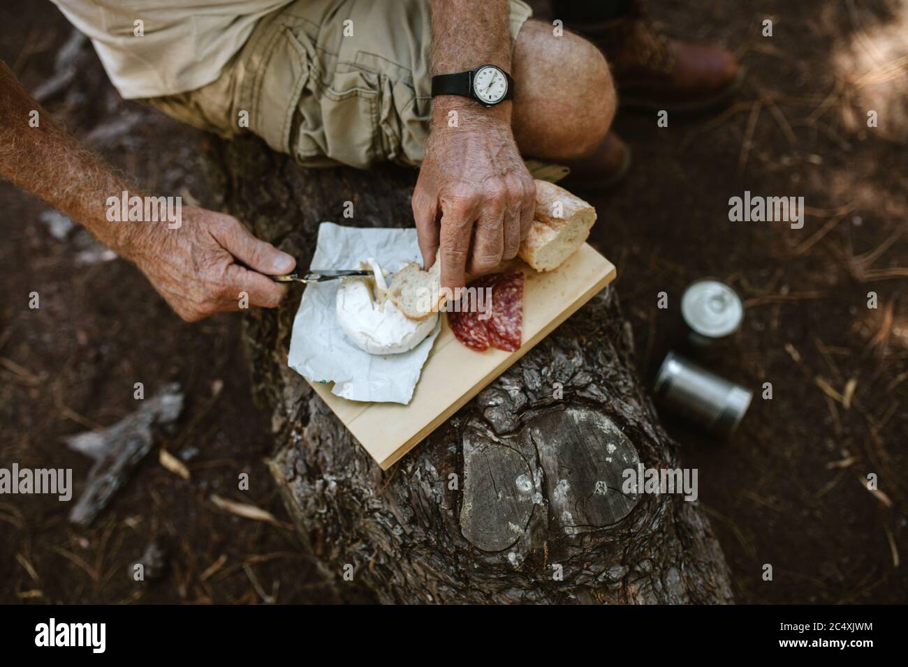 POV Schuss eines älteren Mannes Essen auf dem Campingplatz. Mann auf dem Camping sitzt auf einem Balken und Essen. Stockfoto