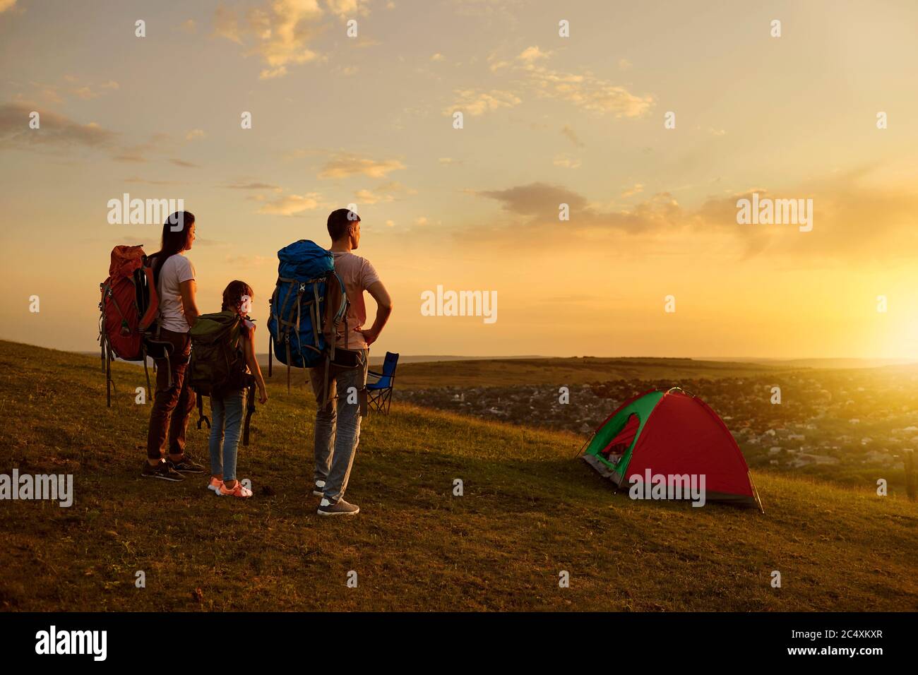 Familiencamping in den Bergen. Eltern und Kind mit Rucksäcken genießen schönen Sonnenuntergang auf dem Campingplatz, Kopierer Platz Stockfoto