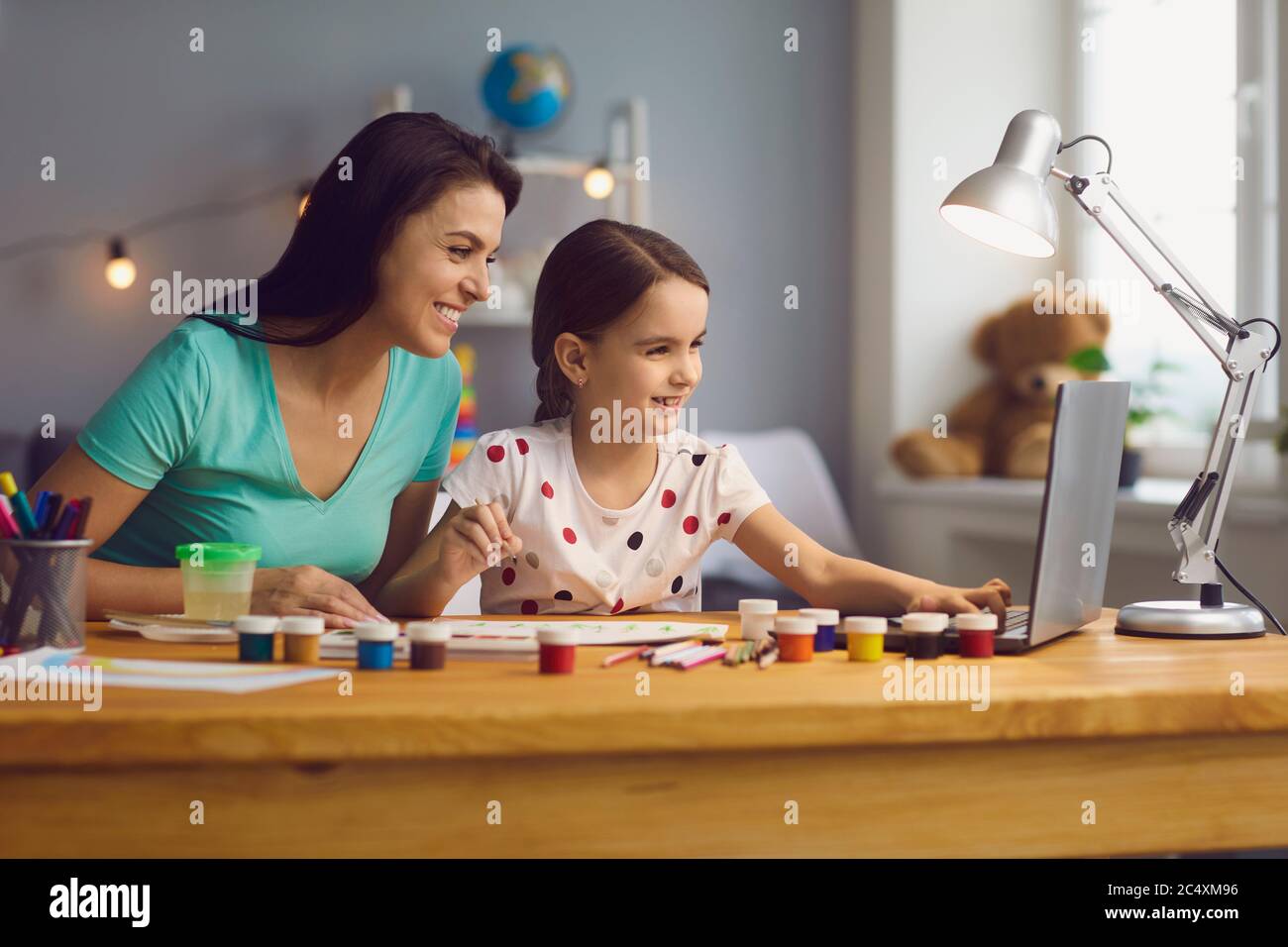 Glückliche Mutter hilft ihr niedliche Tochter Studie online zu Hause. Eltern und Kinder beobachten gemeinsam den Kunstunterricht auf dem Laptop Stockfoto