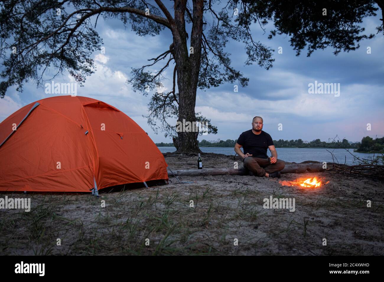 Der Typ auf Selbstisolierung sitzt in der Nähe eines Lagerfeuerzeltes Stockfoto