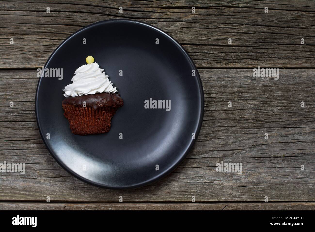 Ein Cupcake, gekrönt mit Schlagsahne und verziert mit einem Knopf-förmigen Süßigkeiten, wurde vertikal geschnitten und auf einem Teller auf verwitterten Holzplanken platziert. Stockfoto
