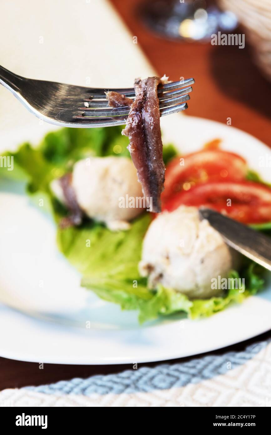Sardelle auf Gabel mit geräucherter Fischpastete und Salat Vorspeise im Hintergrund. Mediterrane Küche, Gourmet-Essen und Reisekonzepte Stockfoto