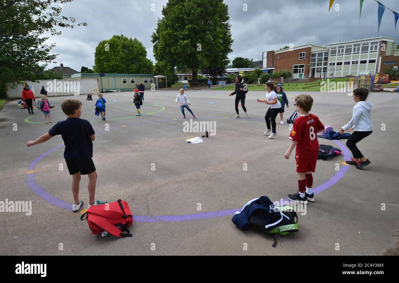 Kinder tanzen auf einem maßvollen und gemalten sozial distanzierten Kreis auf dem Spielplatz, während sie darauf warten, von ihren Eltern an der Llanishen Fach Primary School in Cardiff abgeholt zu werden. Stockfoto