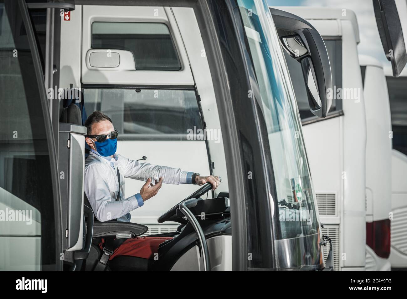 Professionelle Männliche Fahrer Mit Schutzmaske Fahren Coach Bus Aus Parkplatz. Stockfoto