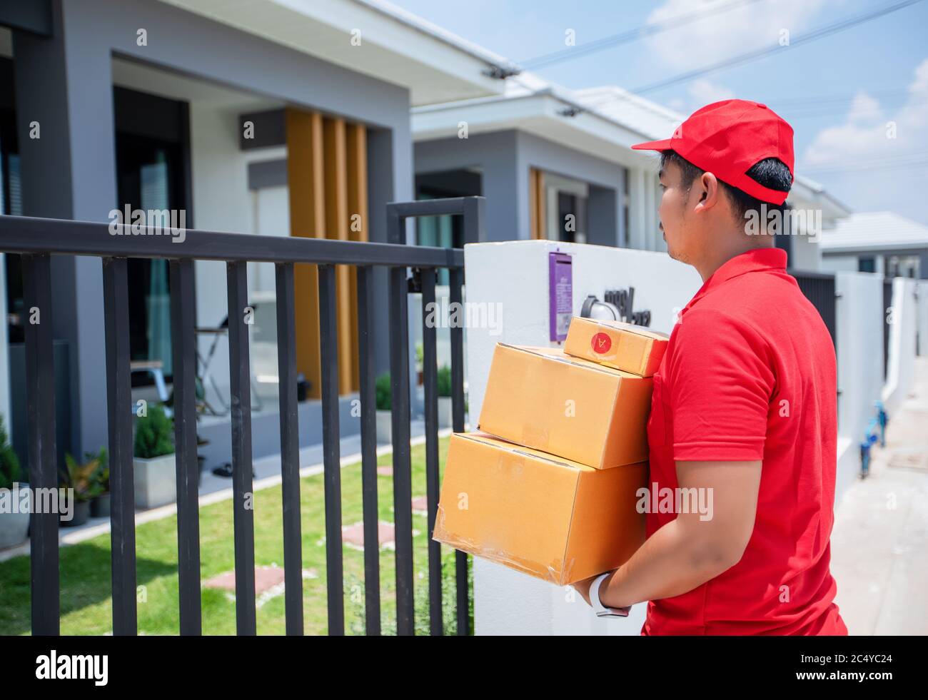 Asiatische Lieferdienstleute tragen eine rote Uniform mit einer roten Kappe und Handhabung von Kartons, um die weibliche Kundin vor dem Haus zu geben. Onli Stockfoto