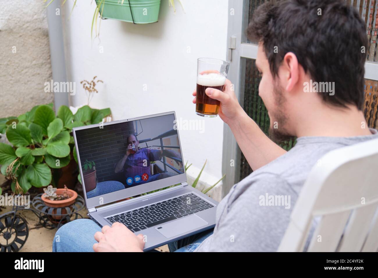 Mann, der mit seinem Vater auf einer Videocall spricht und ein Bier trinkt. Fernkommunikationskonzept. Stockfoto