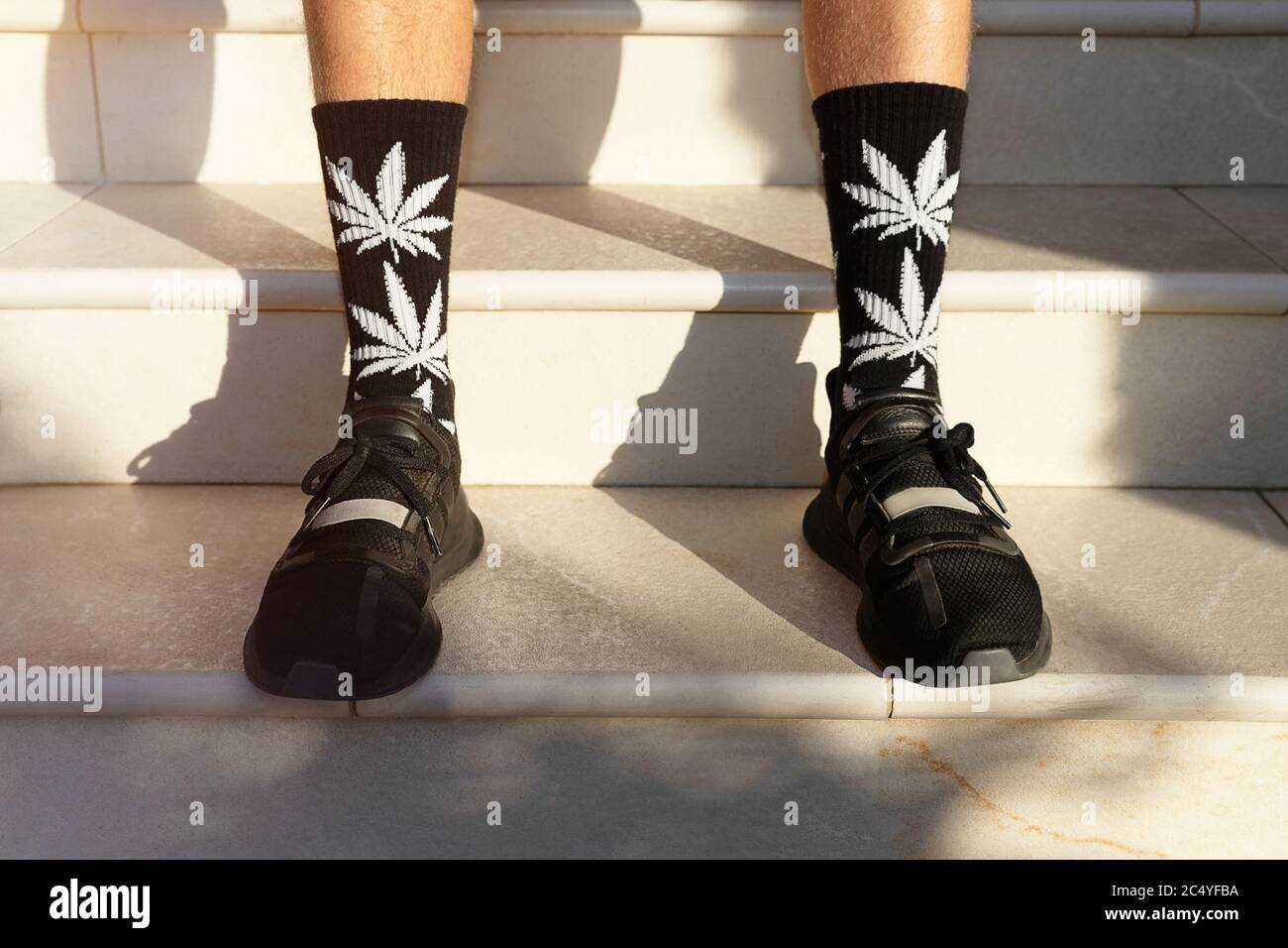 Junge Erwachsene verwenden hohe Socken mit Bildern von Cannabisblättern. Modehintergrund. Stockfoto
