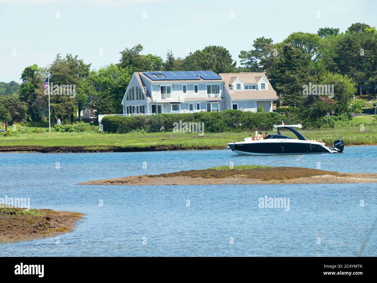 Ein gehobenes Boot, das an einem gehobenen Haus auf Cape Cod, USA vorbeifährt Stockfoto
