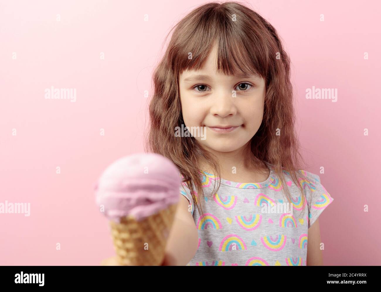 Das fünfjährige Mädchen hält ihre Hand mit Eis aus. Liebenswert kleines Mädchen mit leckeren Eis vor rosa Hintergrund. Selektiver Fokus. Stockfoto