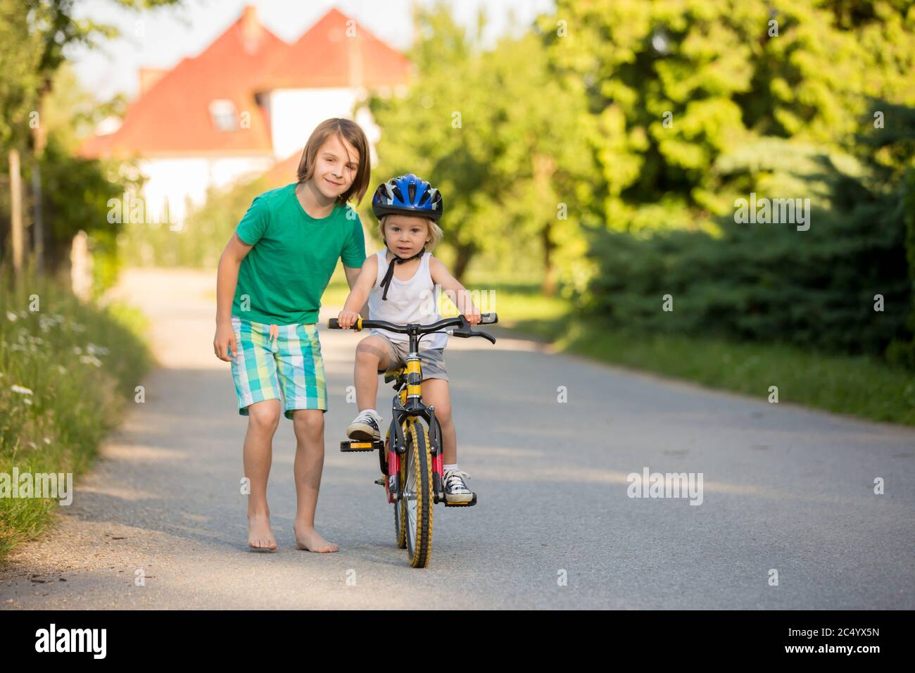 Älterer Bruder, der seinem kleinen Bruder hilft, Fahrrad zu fahren, hält ihn und lehrt ihn Radfahren Stockfoto