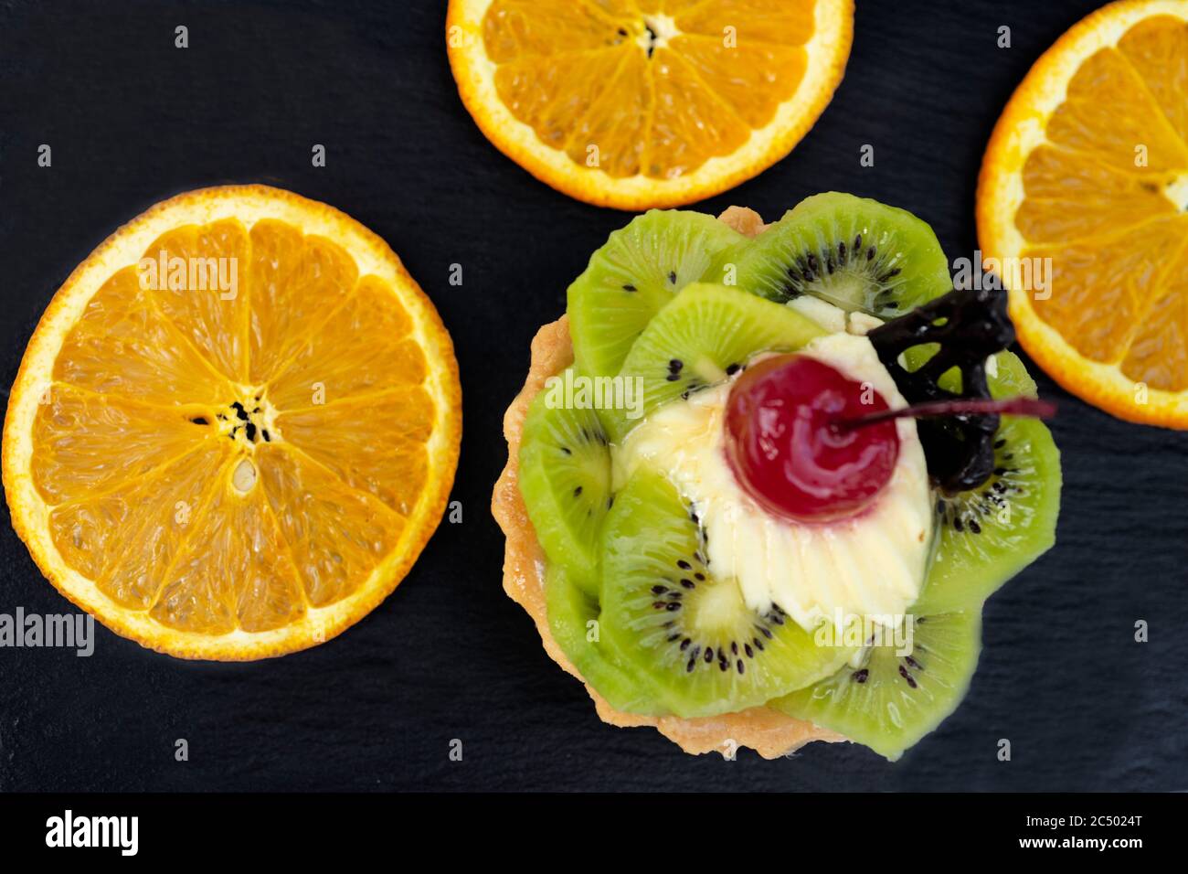 Kuchen mit Kiwi-Kirschen und Pudding, in der Nähe von Jrange-Scheiben. Schwarzer Hintergrund Stockfoto