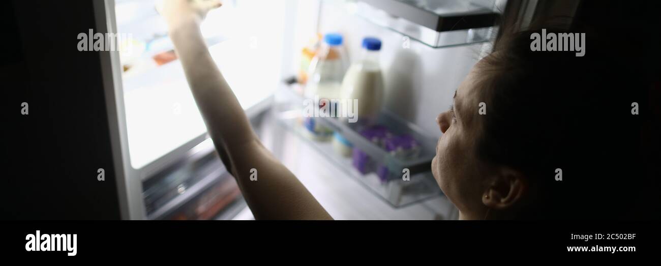 Frau in der Nacht geöffnet Kühlschrank und nimmt Essen Stockfoto