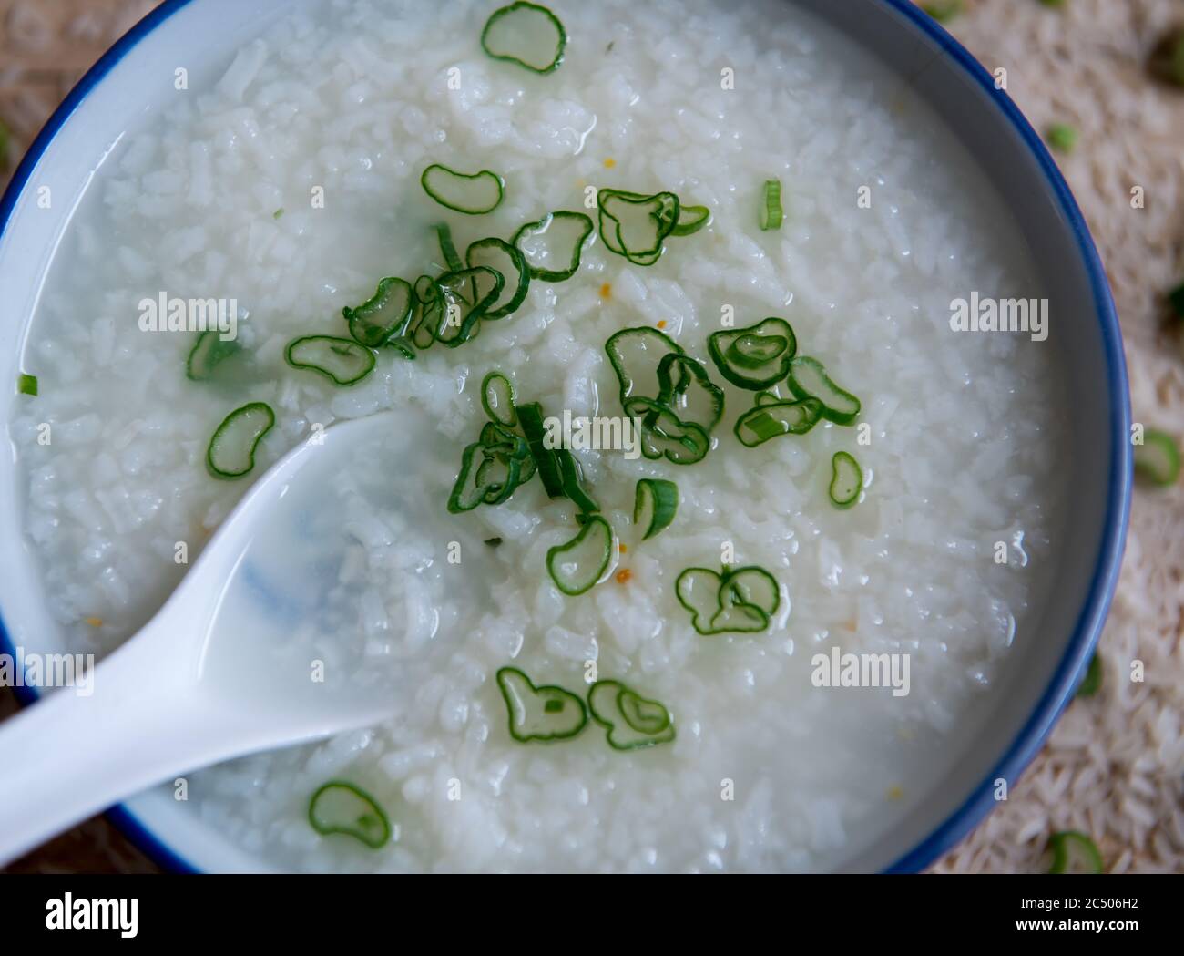 Einfacher Reis Congee, Reisbrei, mit einem Spritzer gehackter Frühlingszwiebel darauf serviert in einem chinesischen Bogen mit Löffel. Stockfoto