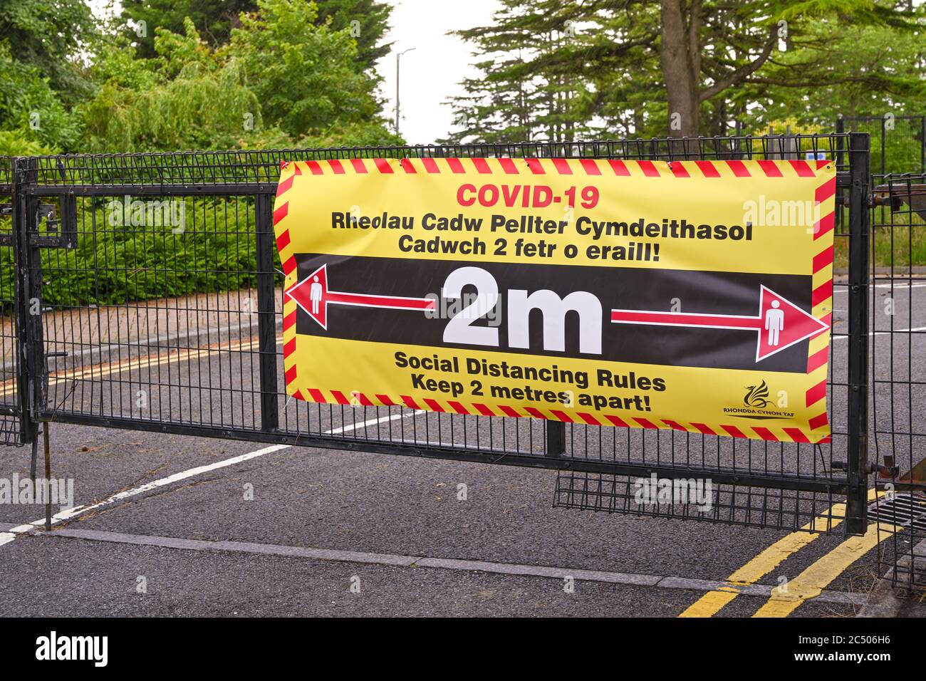 Pontypridd, Wales - Juni 2020: Schulen in Wales wieder eröffnet 29 Juni. Zweisprachiges Schild am Schultor, das die Menschen auffordert, soziale Distanzierungen zu beobachten Stockfoto