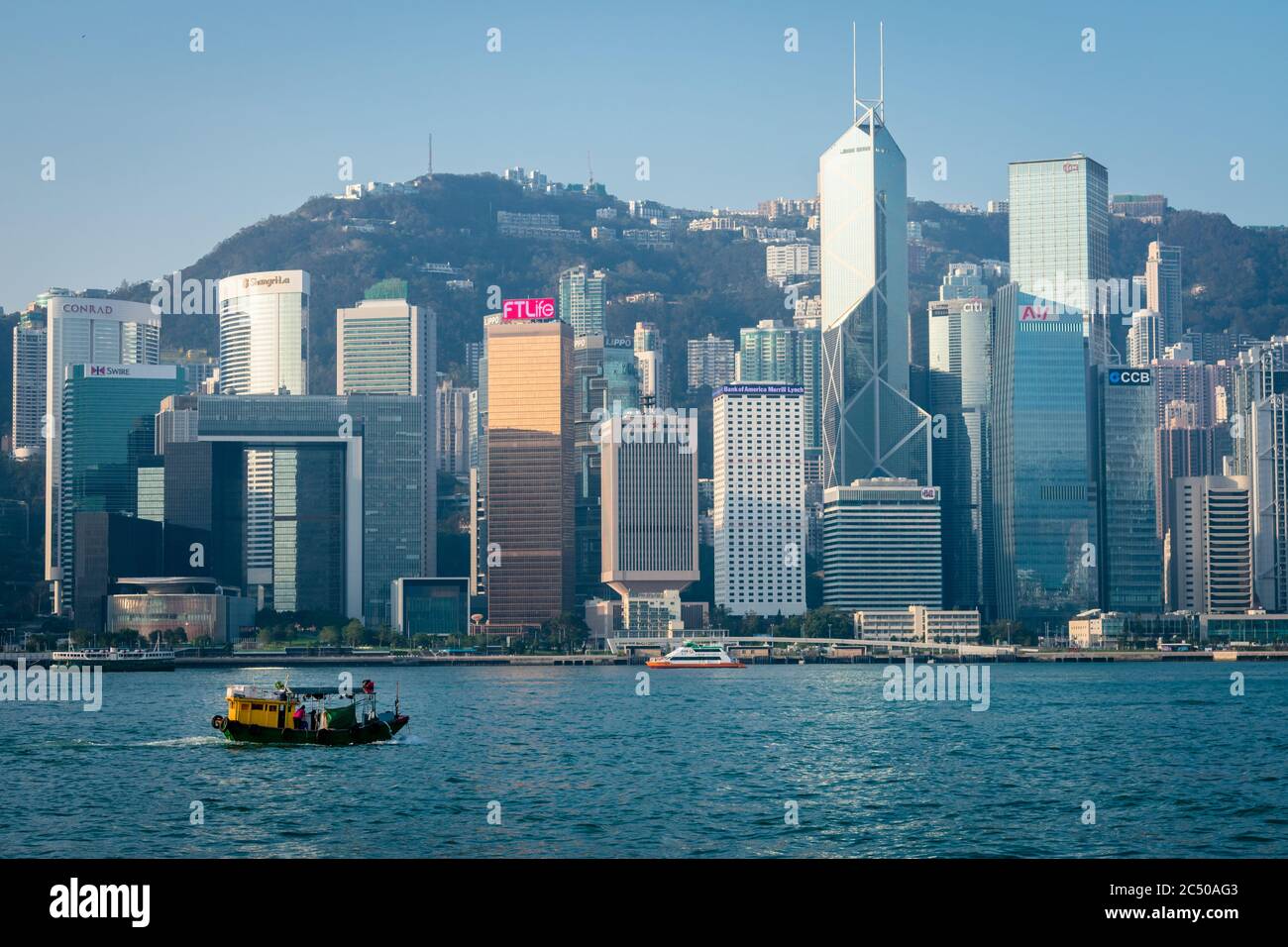 Die Küste der Insel Hongkong mit ihren überfüllten Wolkenkratzern und einem traditionellen Segelschiff, das am Hafen vorbeifährt. Stockfoto