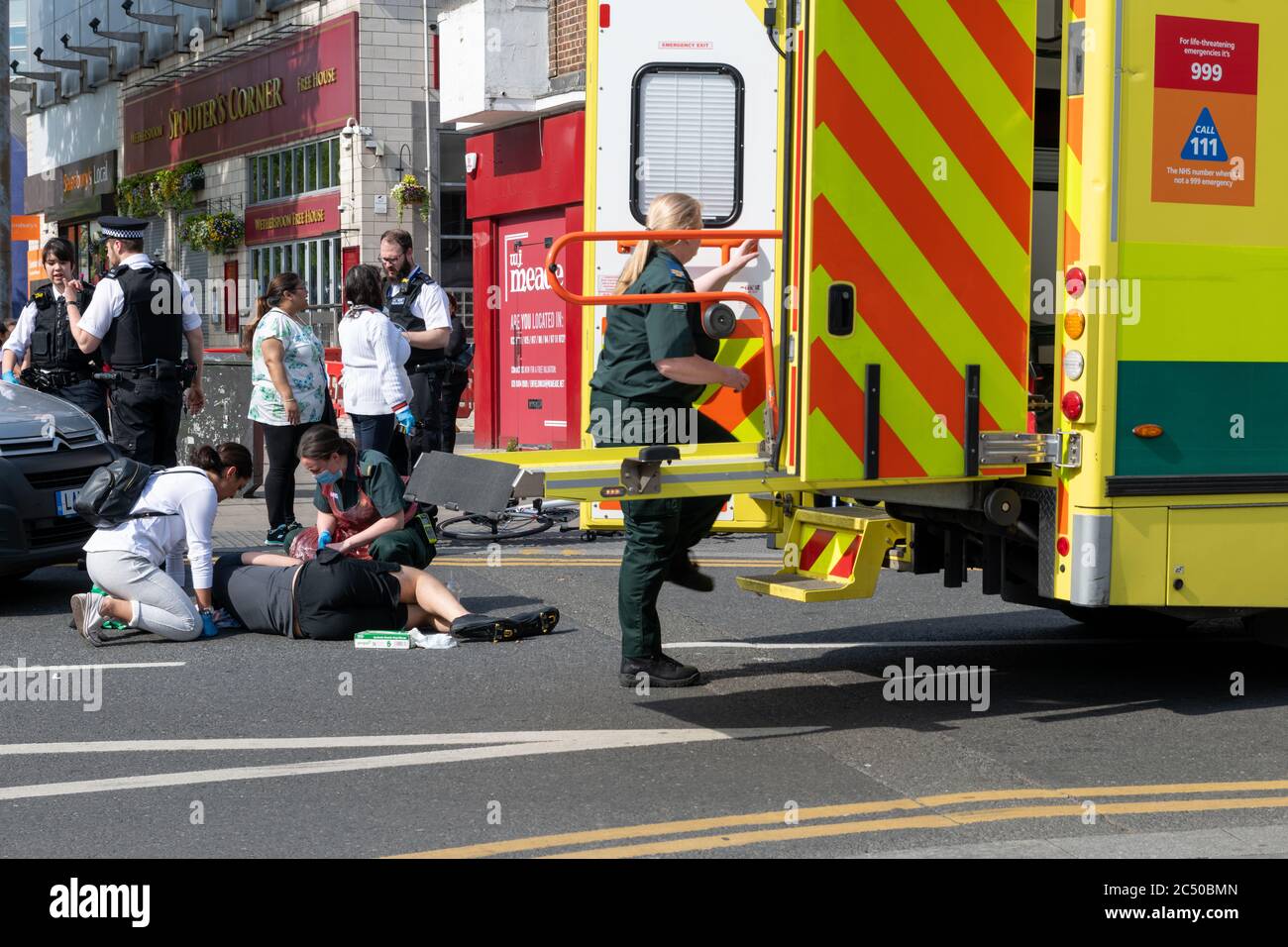 Ein Heimlieferer Radfahrer bei einem Unfall verletzt und auf der Straße mit Polizei und Notarztwagen behandelt. Stockfoto