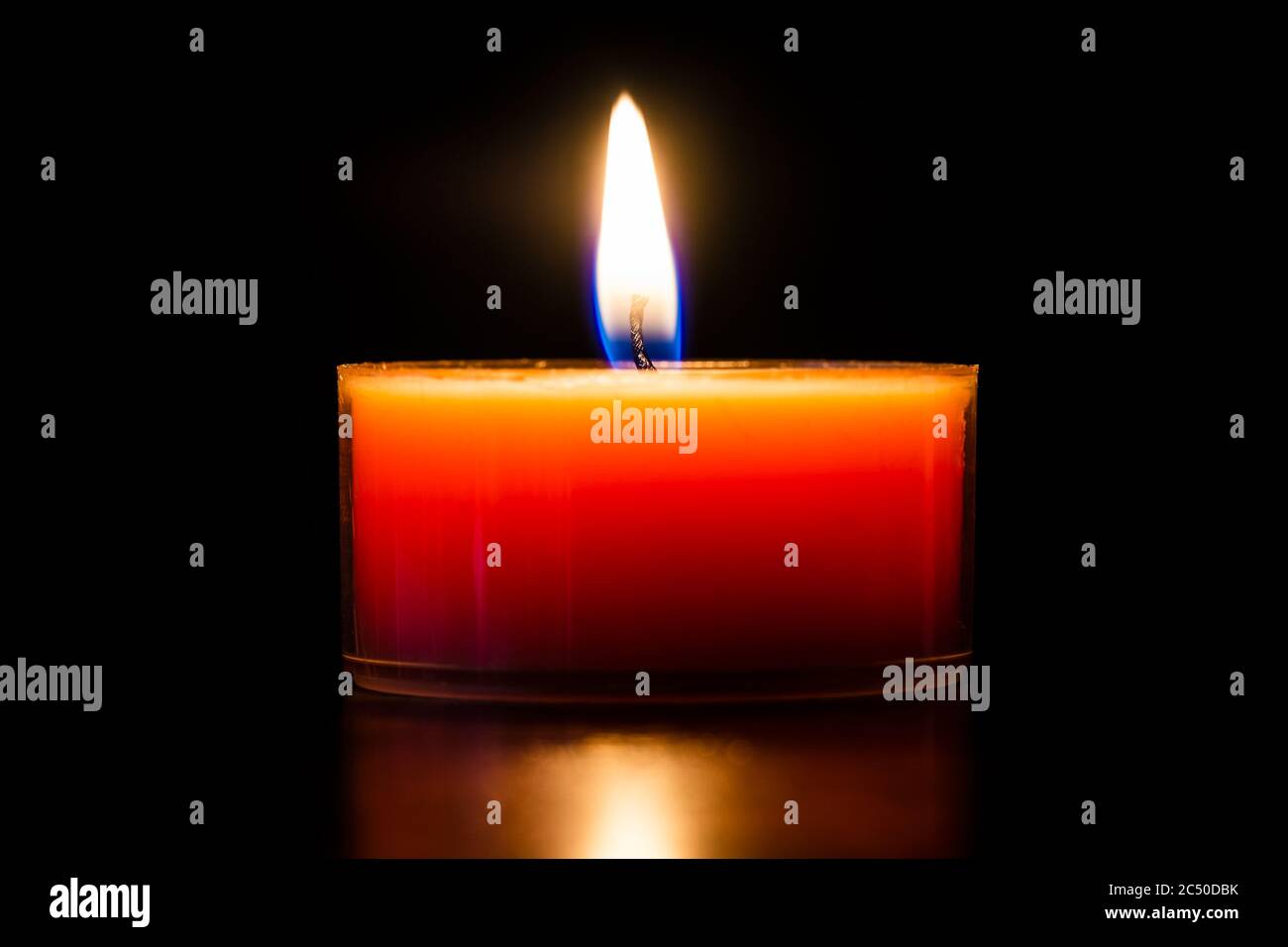 Orange brennende Kerze in einem Glas Teelicht schöne Nahaufnahme isoliert auf schwarz. Stockfoto