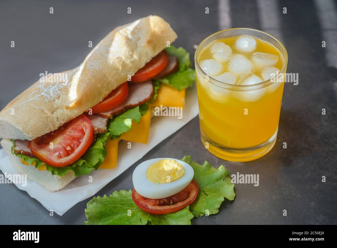 Großes leckeres Sandwich mit Tomatensalat mit Seife und Schinken auf dem Brett. Daneben ist Saft mit Eis in einem Glas. Stockfoto