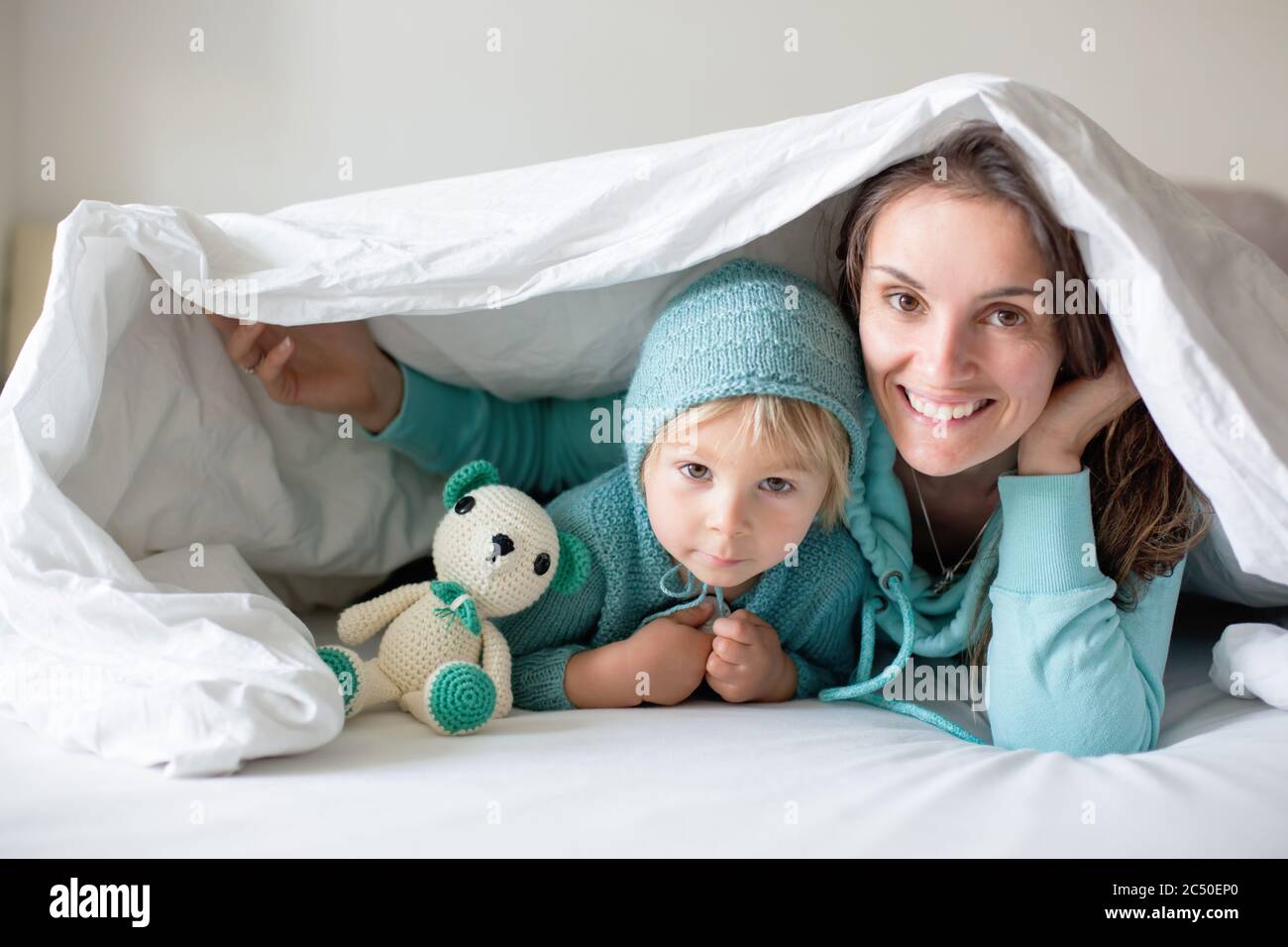 Glückliche Mutter und Kind, Junge, mit passendem Outfit, im Bett liegend, glücklich lächelnd, umarmend und versteckt unter der Decke Stockfoto