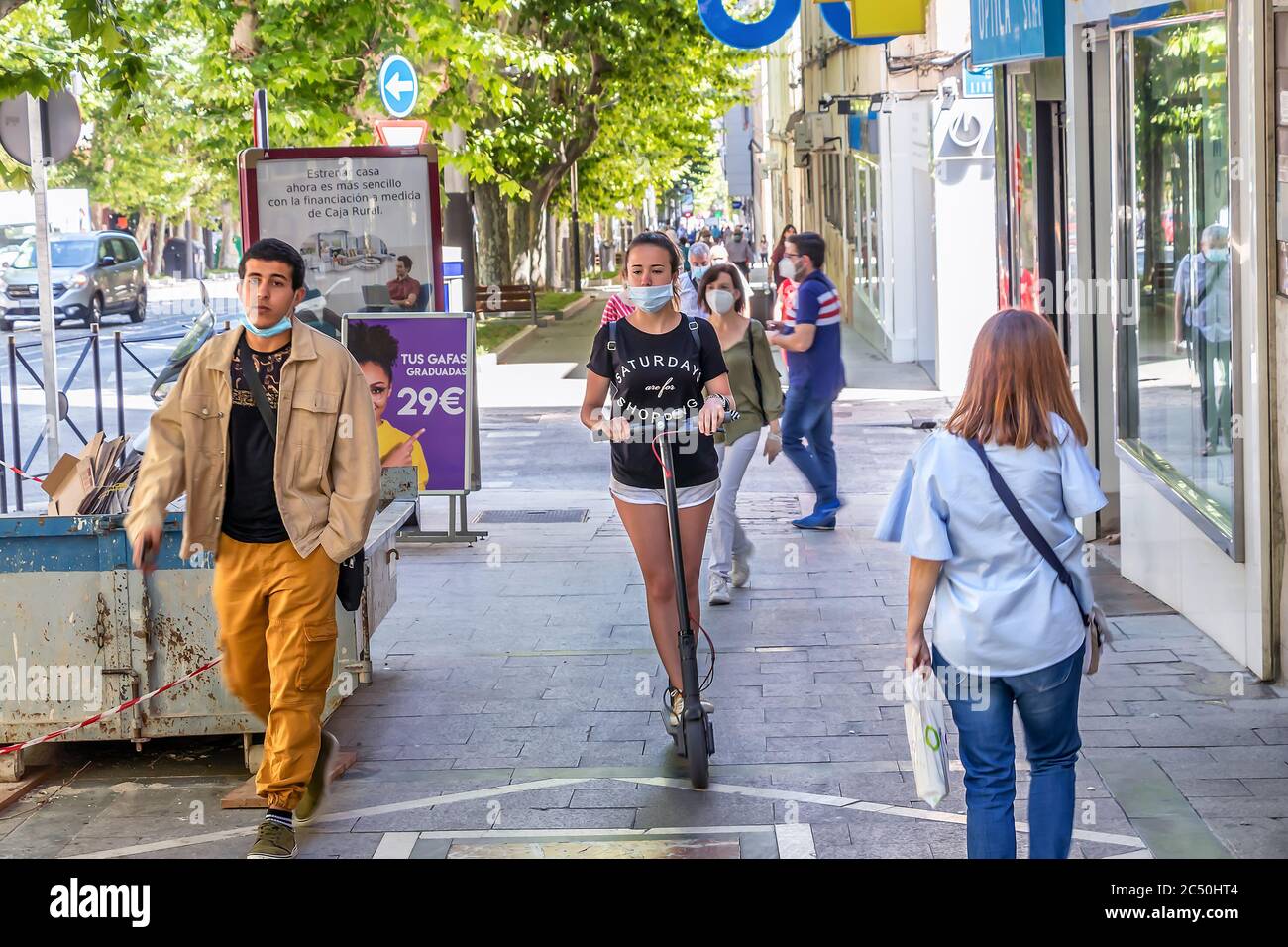 Jaen, Spanien - 18. Juni 2020: Junge Frau, die mit einer Schutzmaske auf einem Elektroroller am Bürgersteig unterwegs ist. Stockfoto