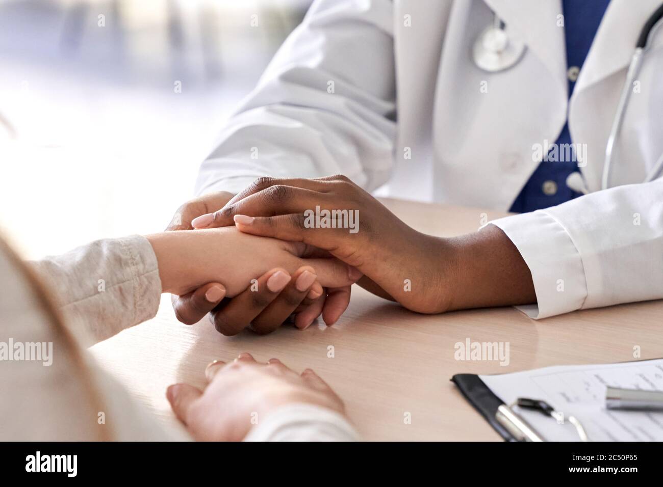 Afrikanischer Arzt hält Hand des kaukasischen Patienten geben Trost, Mitgefühl, Nahaufnahme. Stockfoto