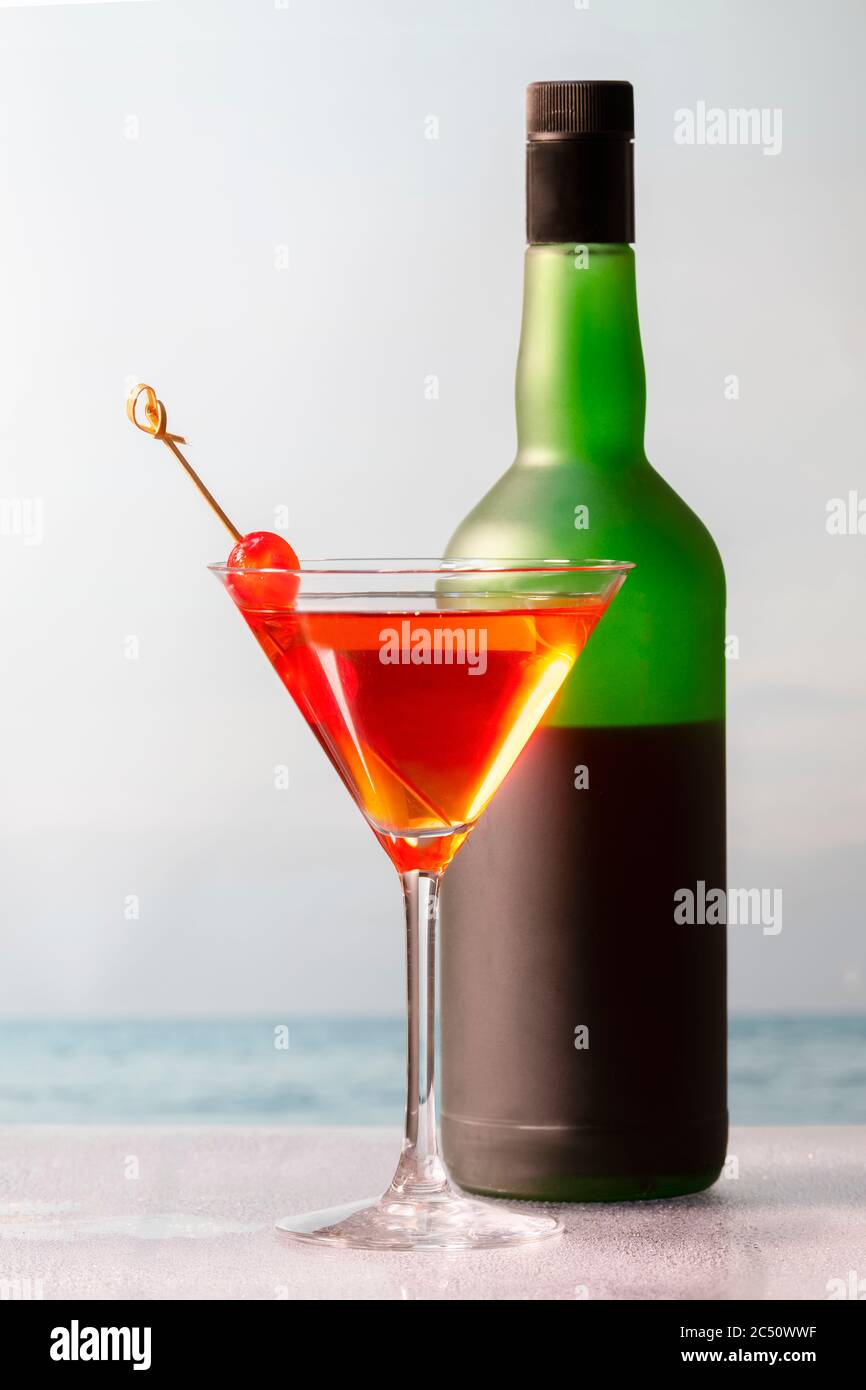 Lecker aussehender hausgemachter Cocktail mit Kirschen in einem martini-Glas vor einer Weinflasche auf einem unfokussieren Hintergrund. Urlaub und Freizeit Konz Stockfoto