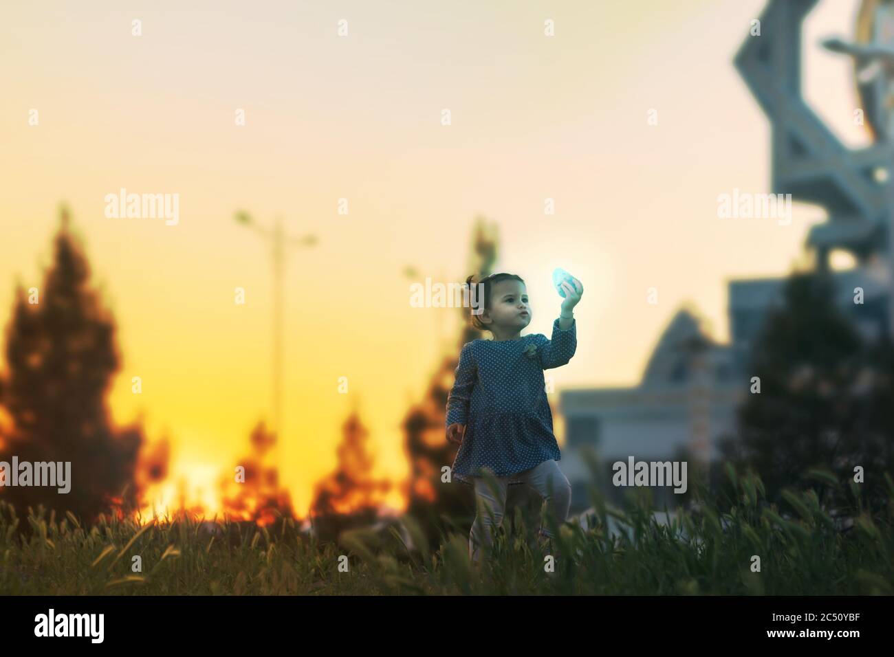 Ein kleines Mädchen fand während des Sonnenuntergangs einen glühenden Stein in einem Grasfeld Stockfoto