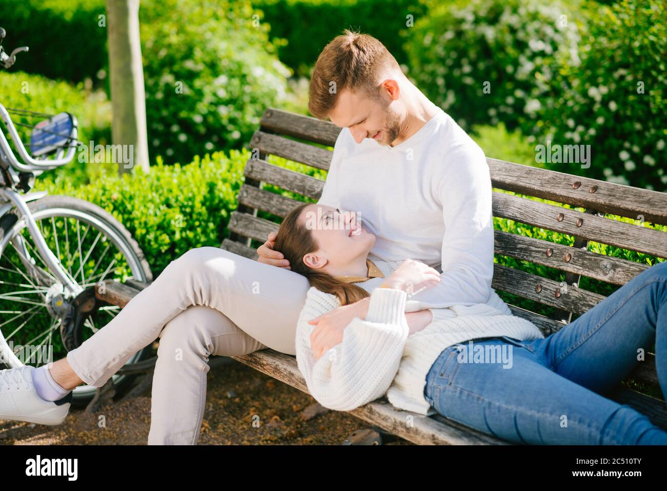 Mann, der auf einer Bank sitzt und eine liegende Frau umarmt Stockfoto