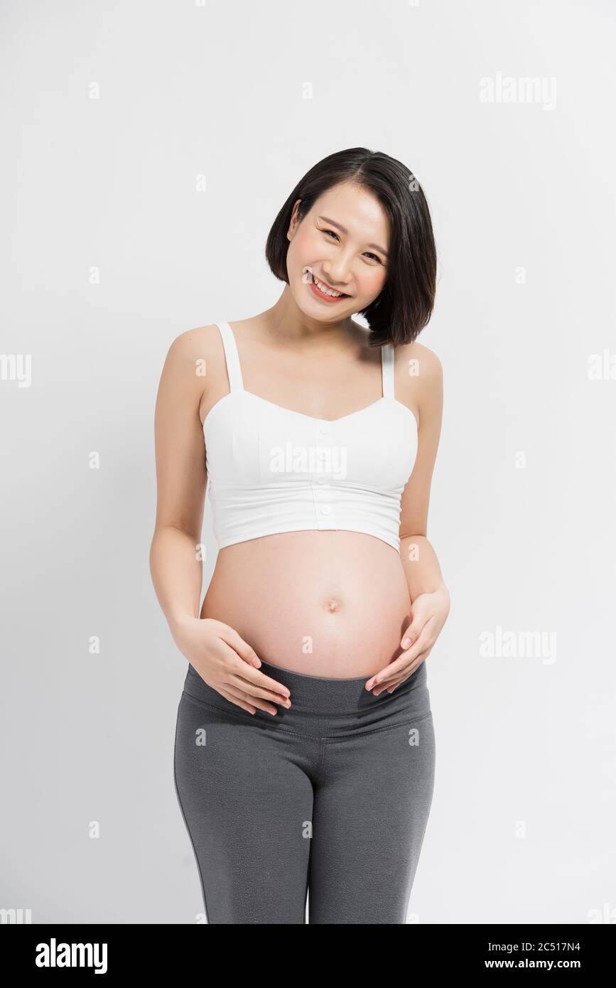 Schwangere Frau im Kleid hält die Hände auf dem Bauch auf einem weißen Hintergrund Stockfoto
