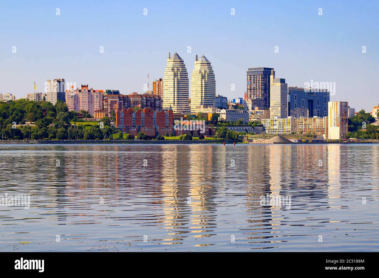 Große Stadt am Ufer breiten Fluss. Schöne moderne Türme, Gebäude, Wolkenkratzer spiegeln sich am Sommermorgen im Wasser. Ukrainische Stadt Stockfoto