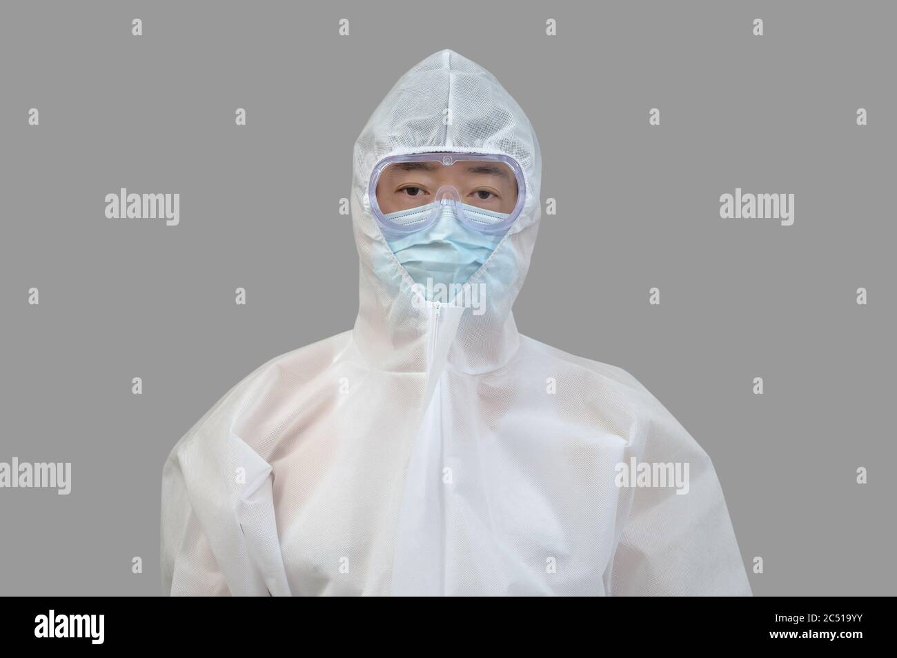 Ein asiatischer Mann, der Schutzanzug, medizinische Masken und eine Brille auf grauem Hintergrund trägt. Stockfoto