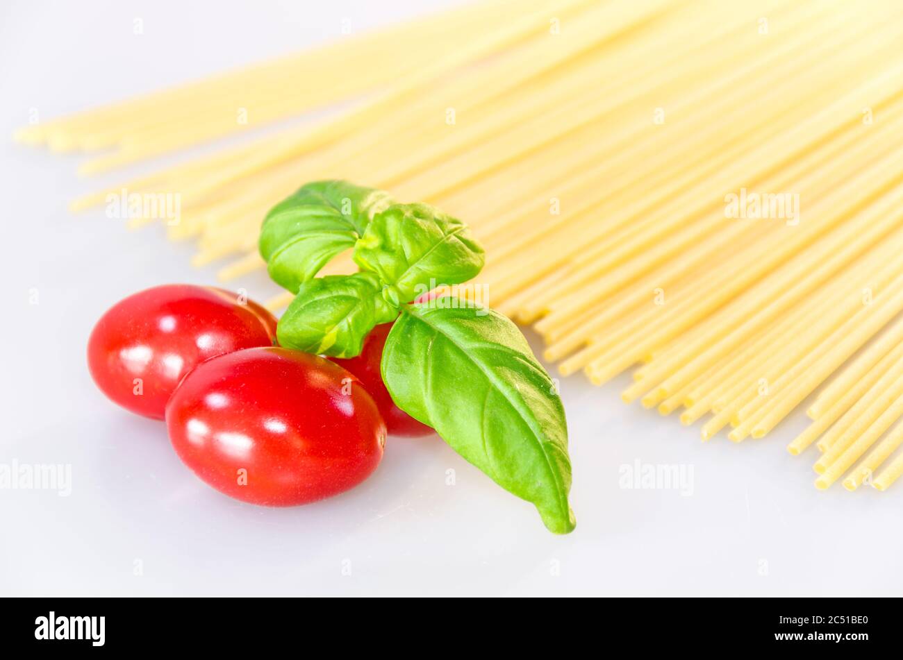Ungekochte Pasta-Spaghetti, rote leckere Tomaten und grüne Basilikumblätter auf weißem Tisch Stockfoto