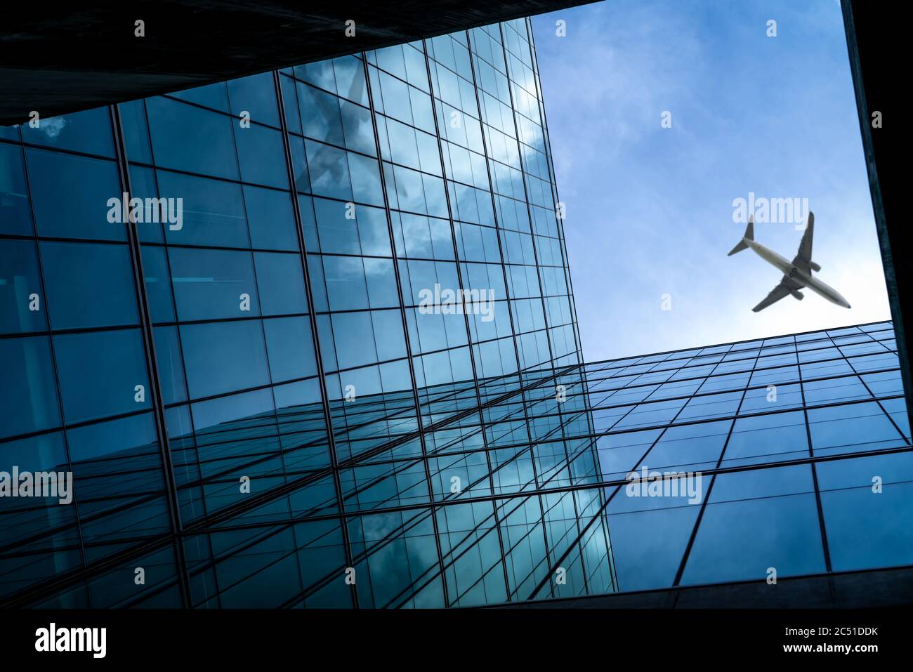 Flugzeug fliegt über dem modernen Bürogebäude aus Glas. Perspektivische Ansicht des futuristischen Geschäftsgebäudes. Außenansicht des Wolkenkratzers. Geschäftsreise. Stockfoto