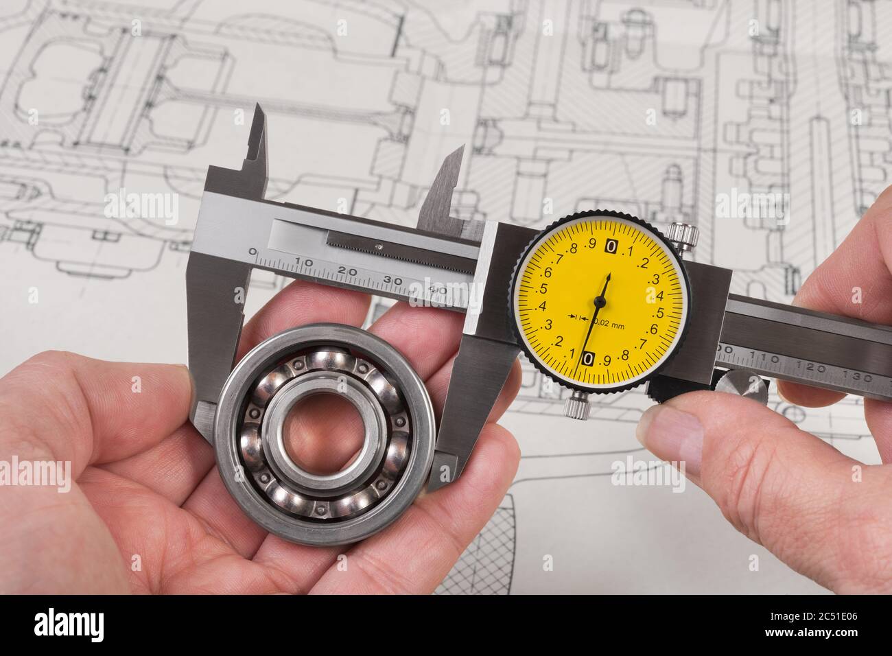 Messung des Stahlkugellagers durch präzisen analogen Bremssattel über der technischen Zeichnung. Messwerkzeug aus Metall mit rundem gelben Zifferblatt in den Händen des Technikers. Stockfoto
