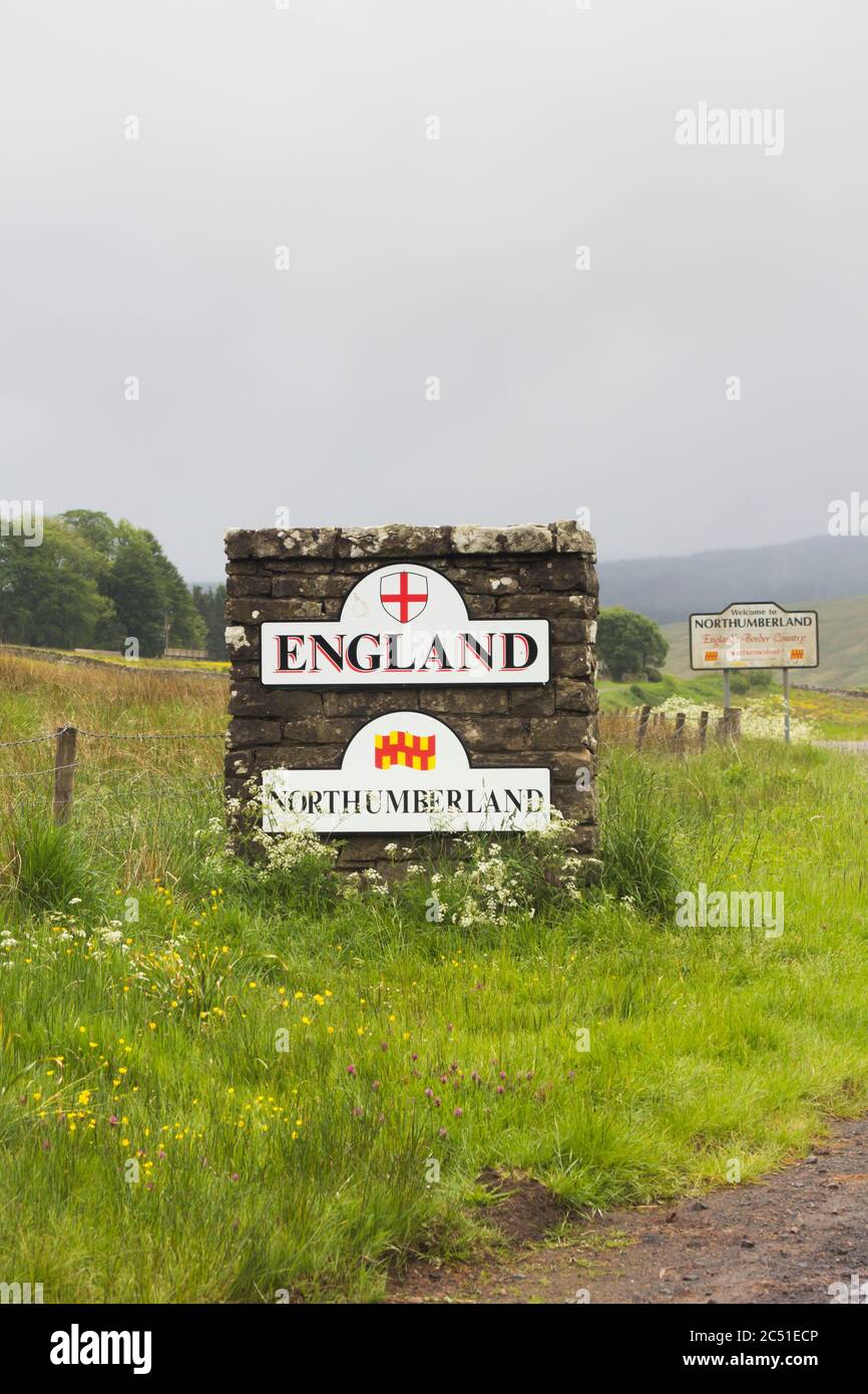 Steinsäule und Schilder, die die Grenze zwischen England und Schottland kennzeichnen, nahe an einer nicht klassifizierten Straße in Deadwater, Kielder, Northumberland an einem trüben und nebligen Tag. Stockfoto