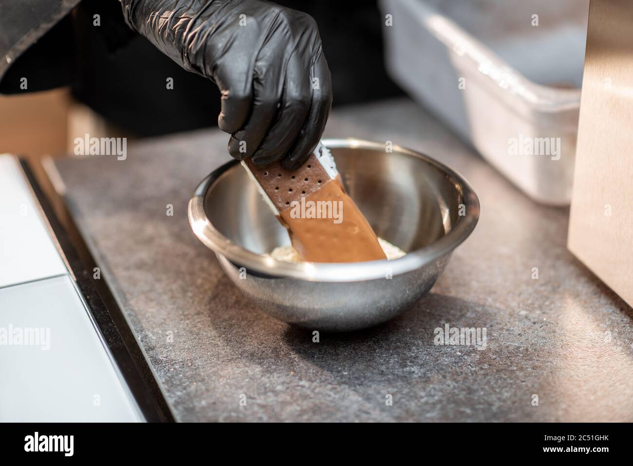 Koch bereitet Schokoladeneis mit Belag im Laden zu, Nahaufnahme Stockfoto