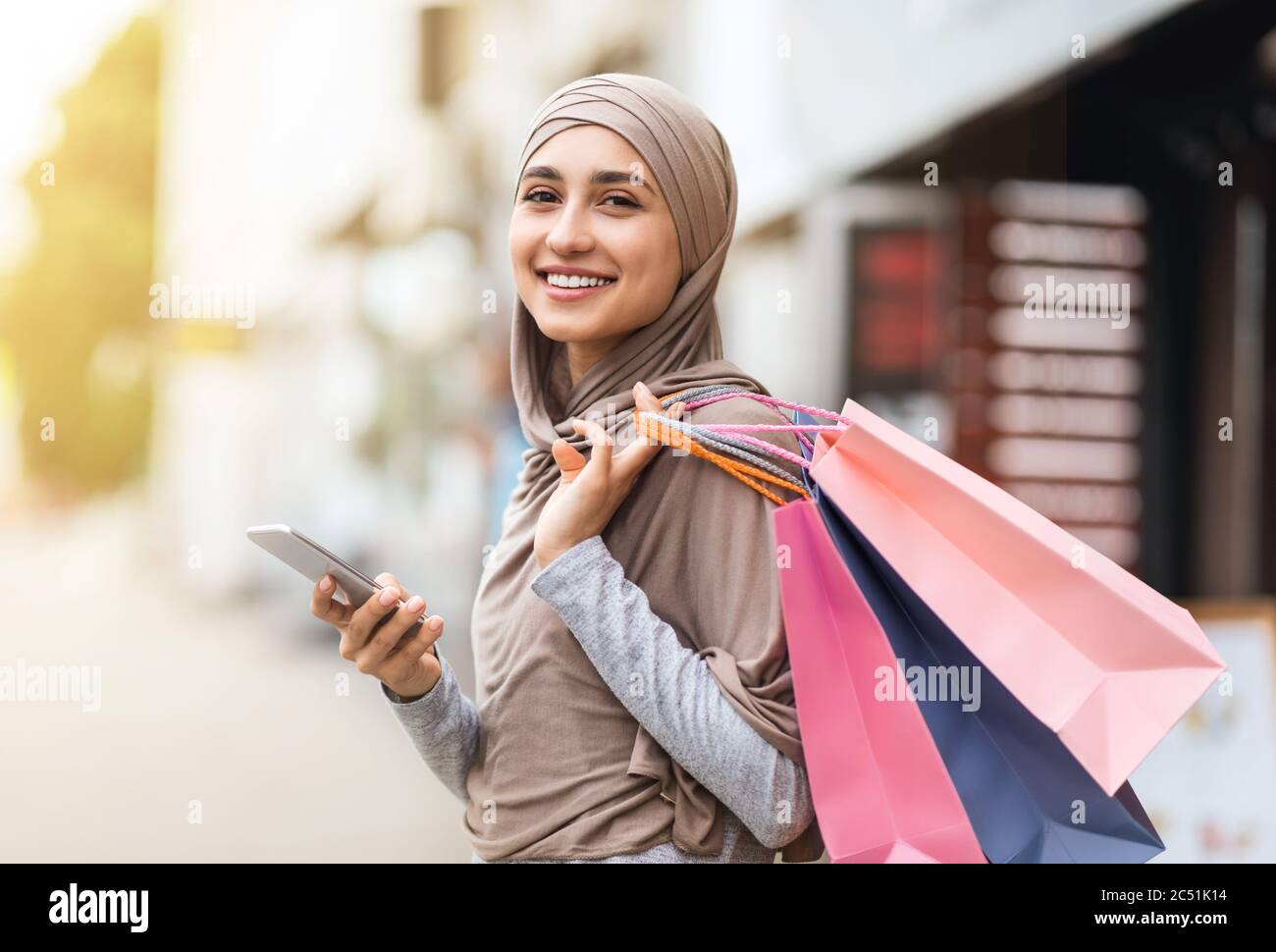 Glückliches Mädchen in Hijab zu Fuß durch die Straße mit Einkaufstaschen Stockfoto